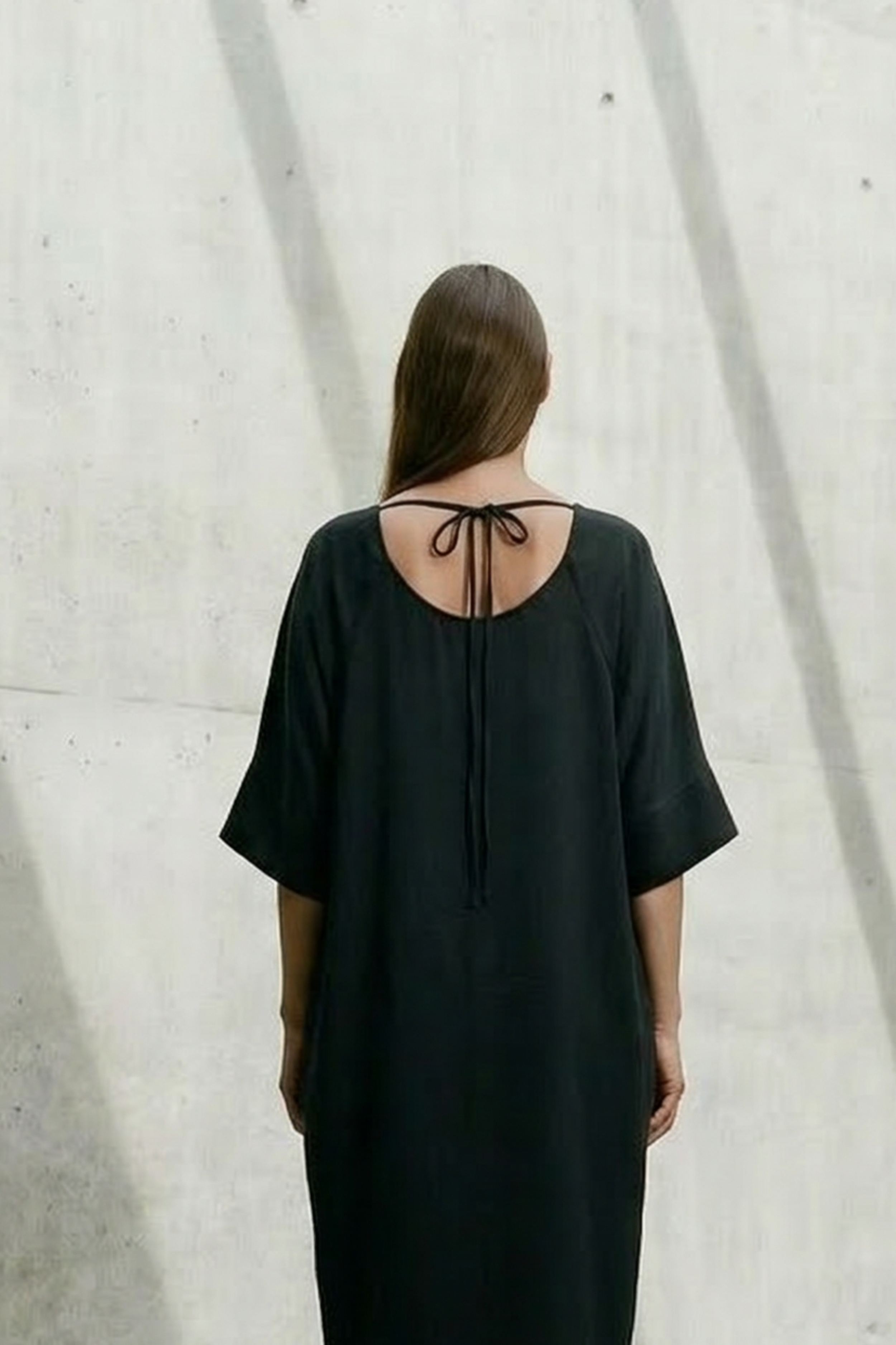 Person wearing a black dress standing in a sunlit concrete room