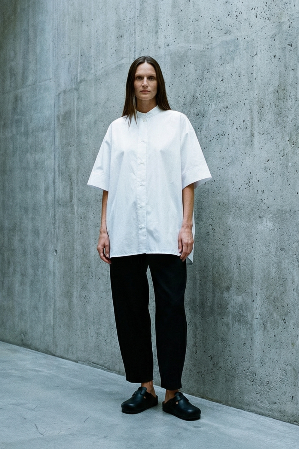 Person wearing a white shirt and black pants standing in a concrete architectural space