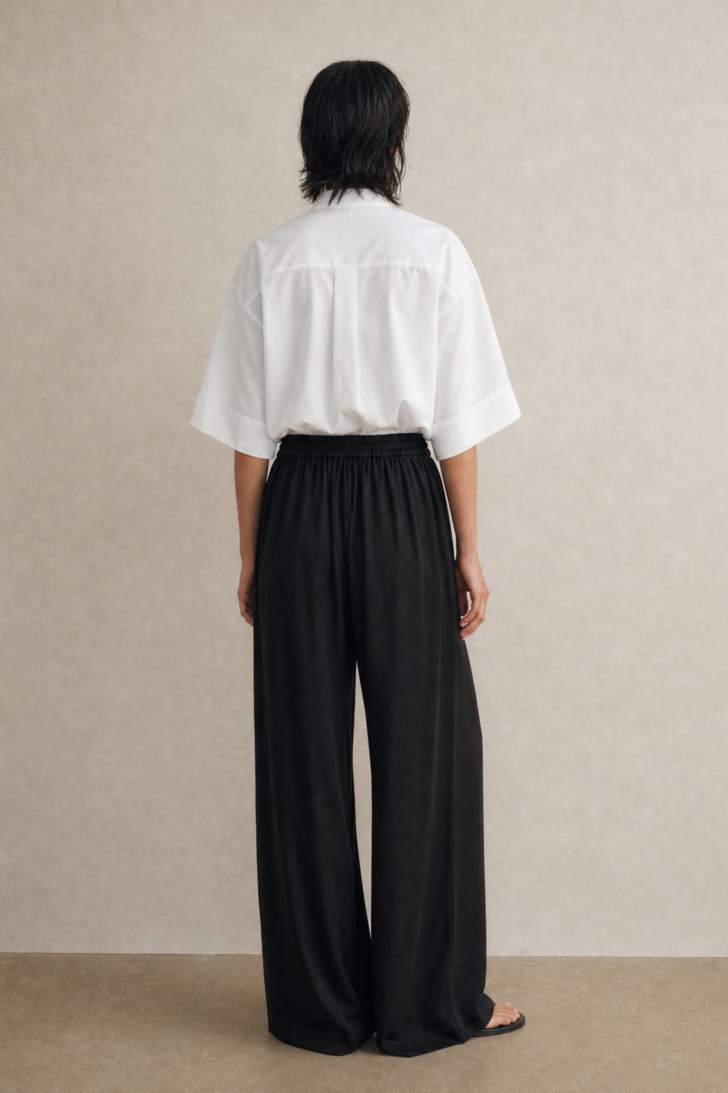 Person wearing a white shirt and black pants against a beige background