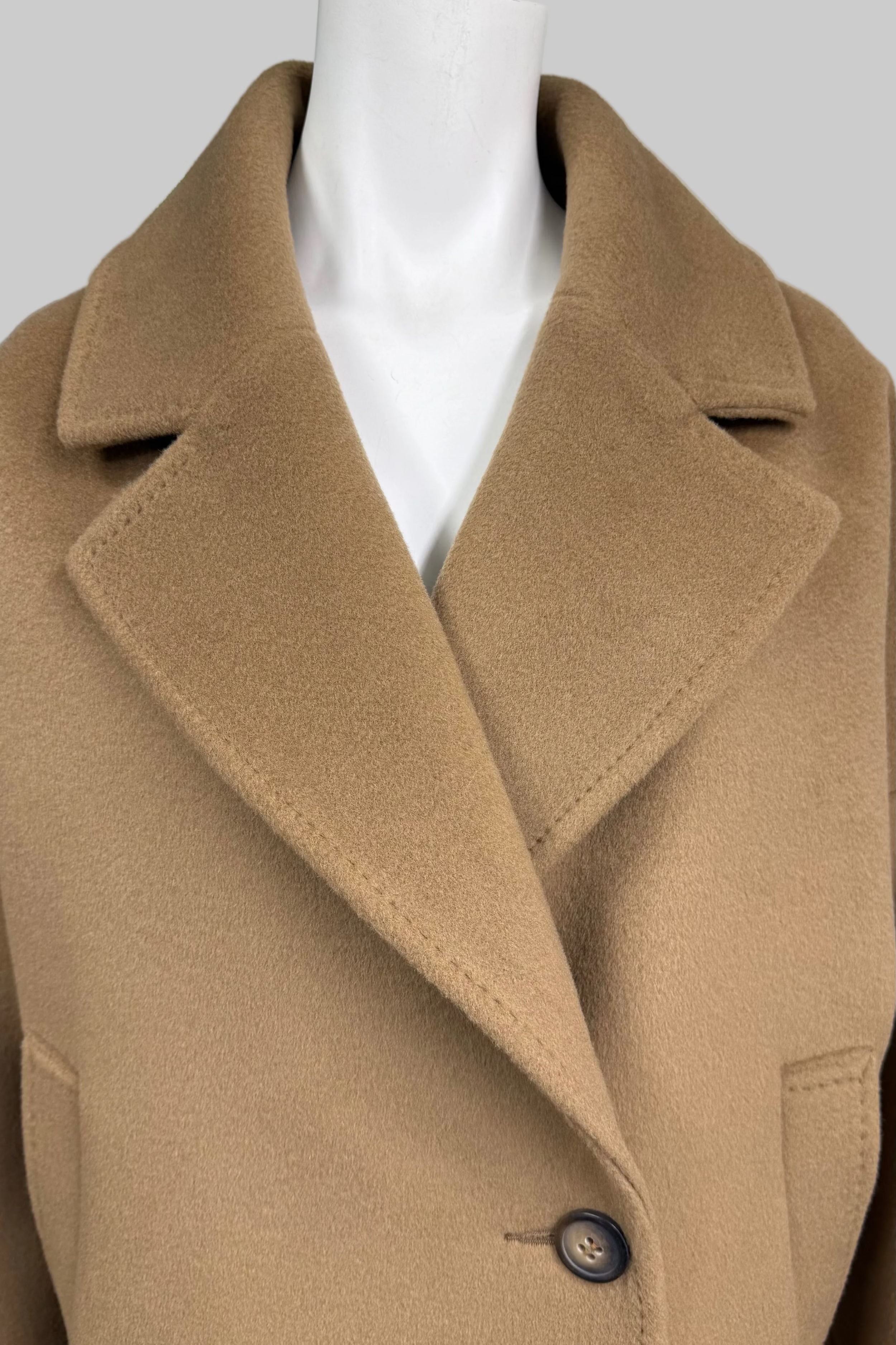 A camel-colored wool coat displayed on a white mannequin torso, featuring a single dark button and a clean collar.