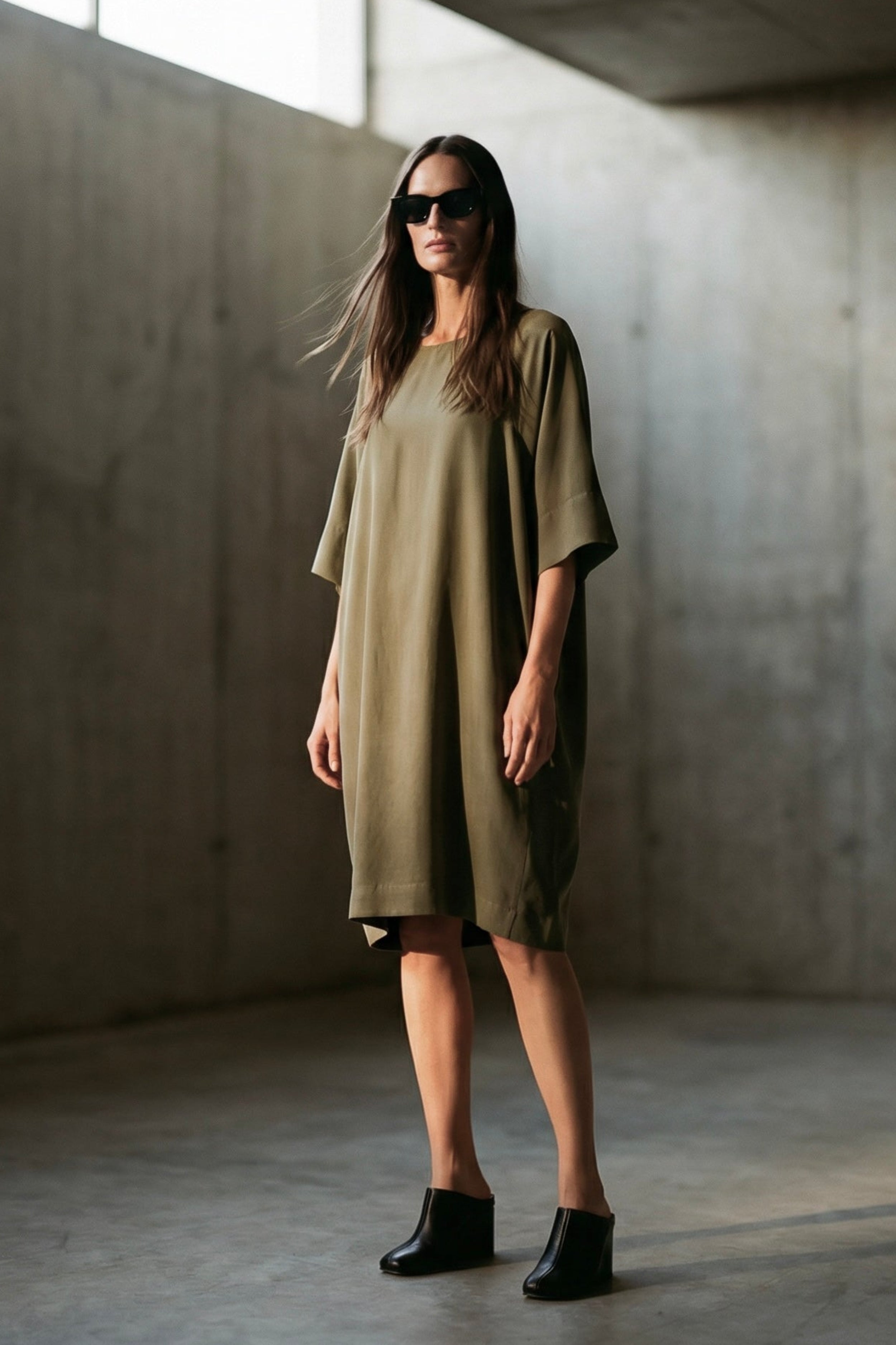 Woman wearing a green dress standing in a dimly lit room with concrete walls.