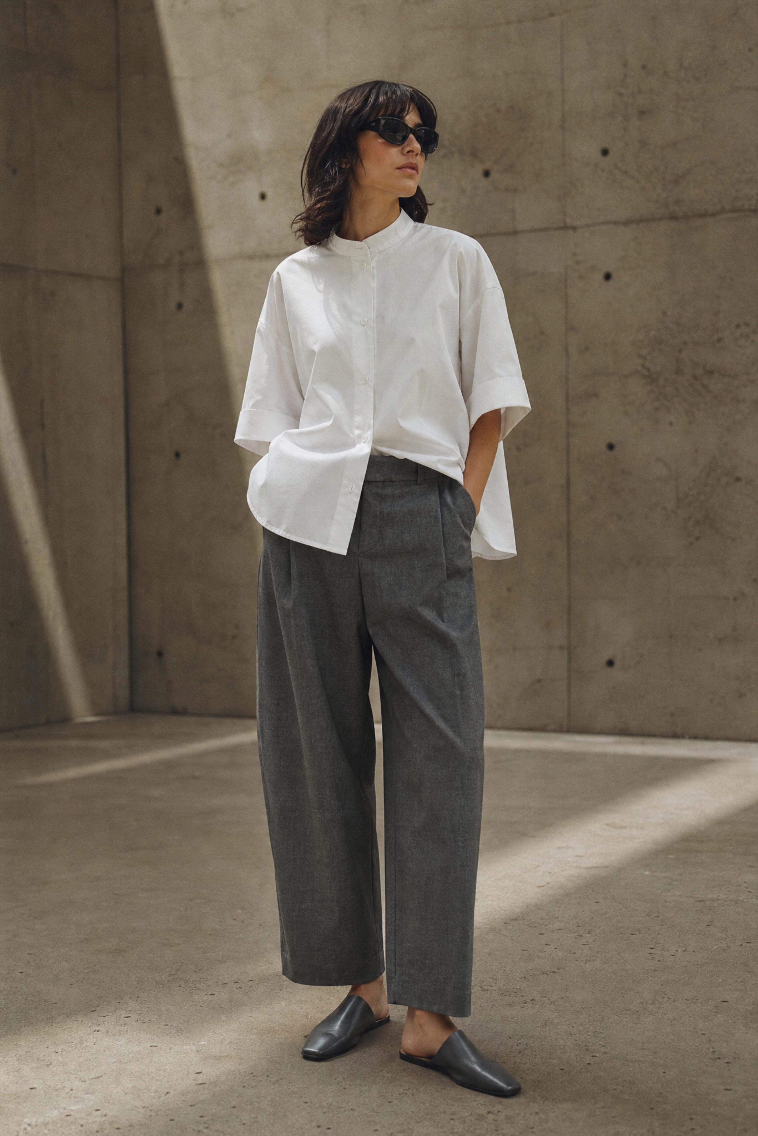 Person wearing a white shirt and gray pants standing against a concrete wall.