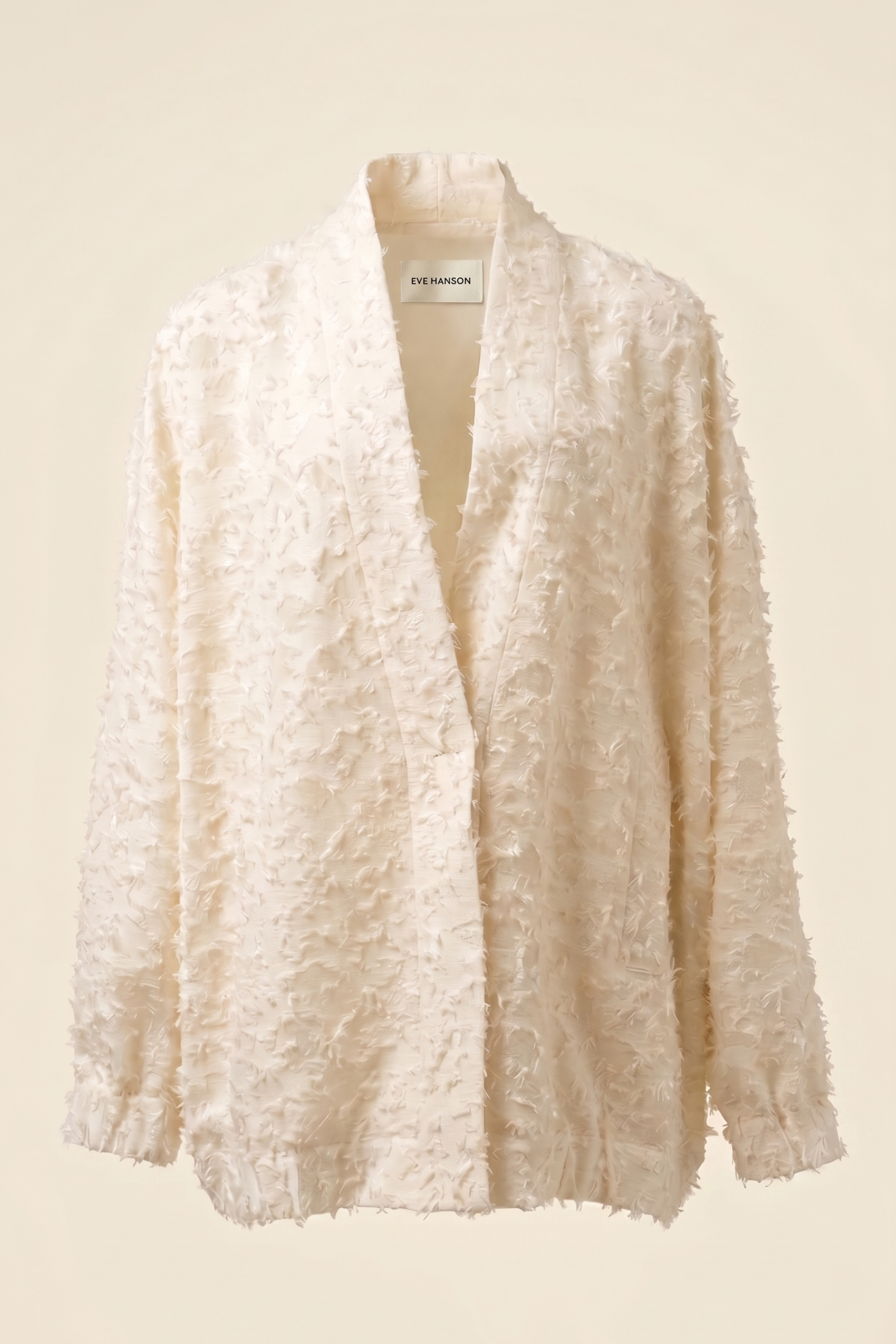 An off-white textured cardigan by Phat Shampons, featuring a fuzzy, crinkled fabric and a split neckline, displayed against a solid cream background.