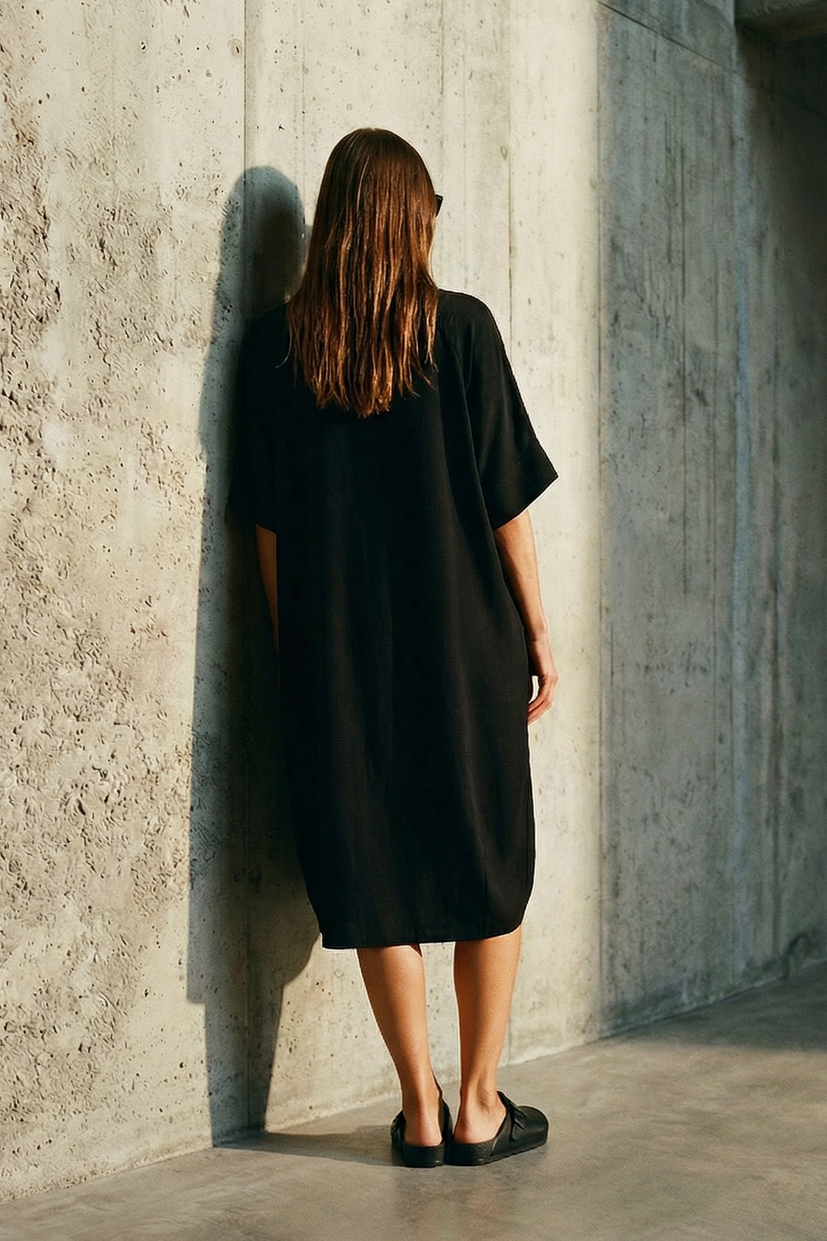 Person wearing a black dress standing in a concrete room