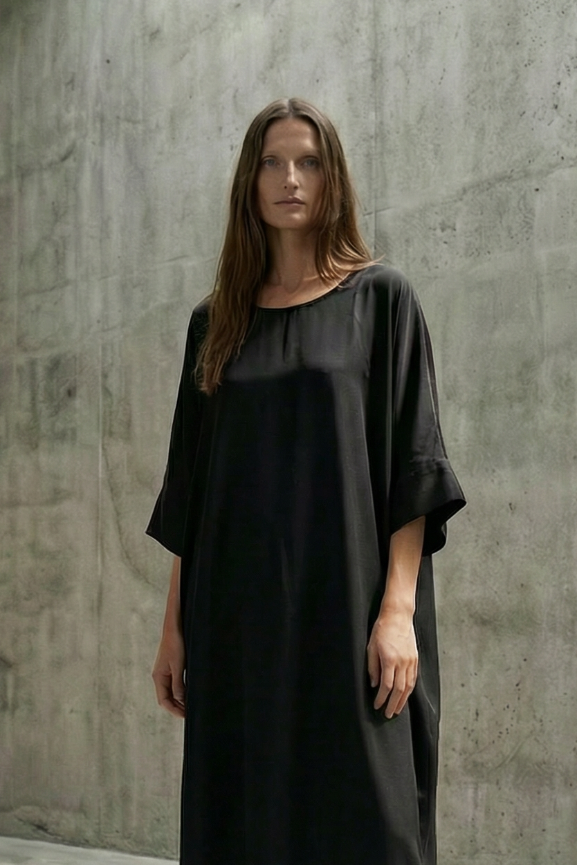 Woman wearing a black dress standing in a concrete room with a high ceiling.