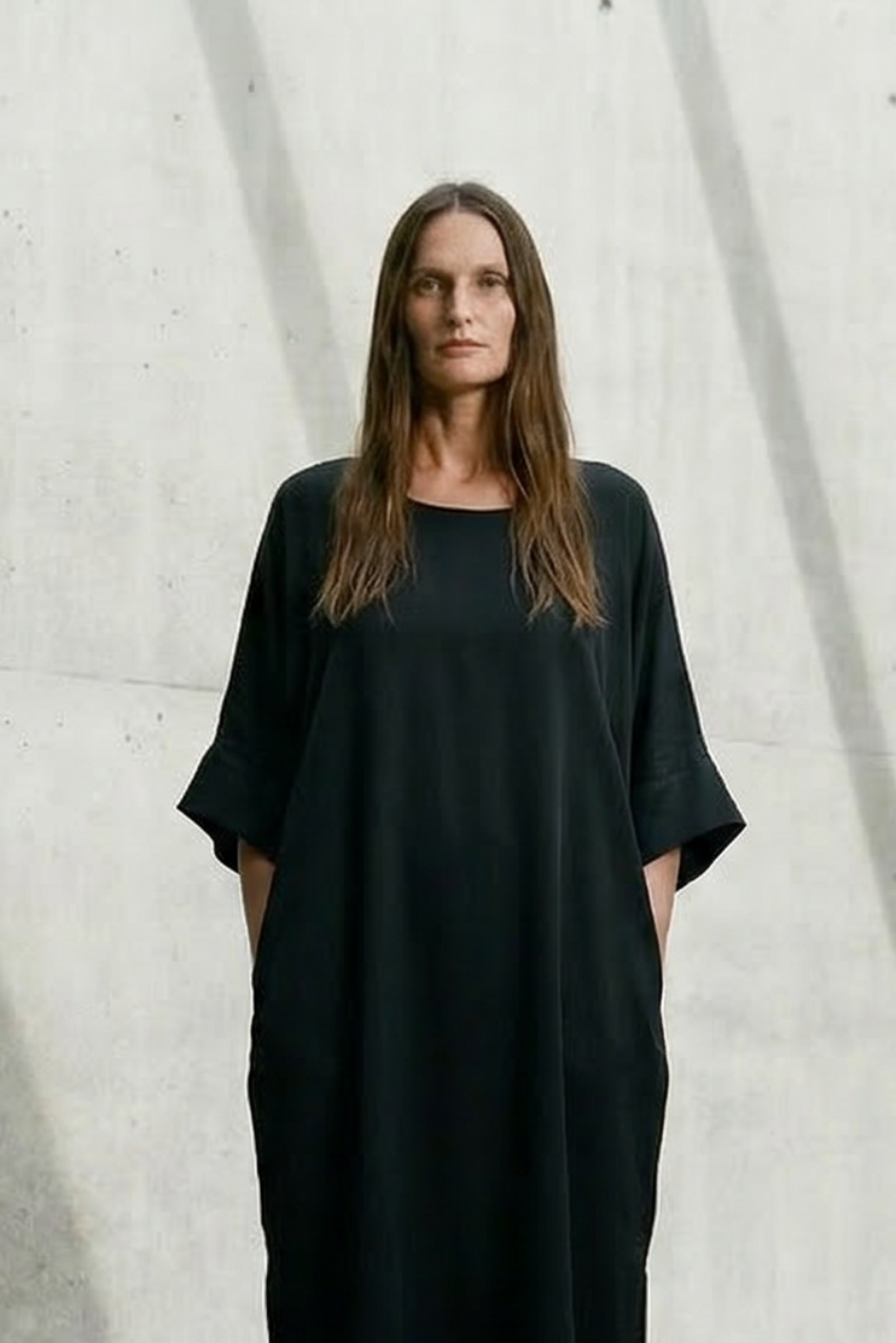 Woman wearing a black dress standing in a modern architectural setting with concrete walls and floor.