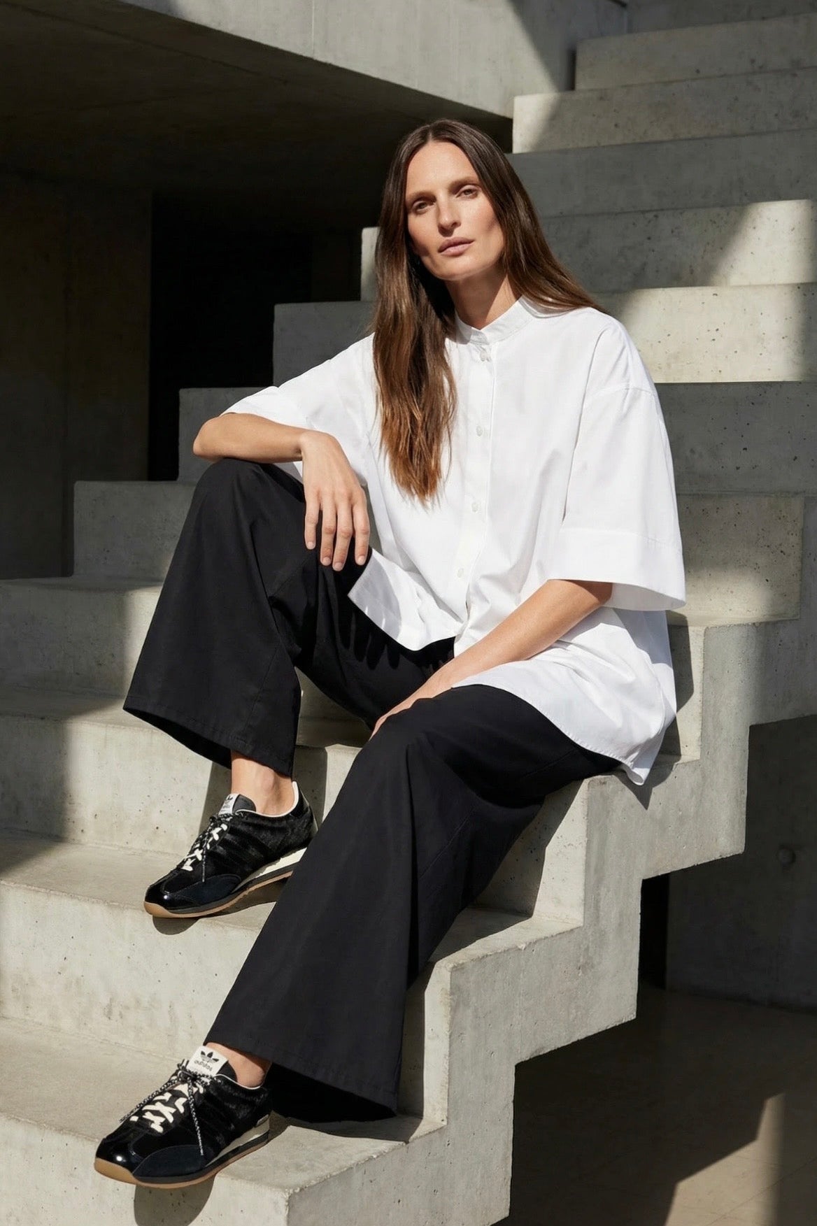 Woman sitting on concrete steps wearing a white shirt and black pants.