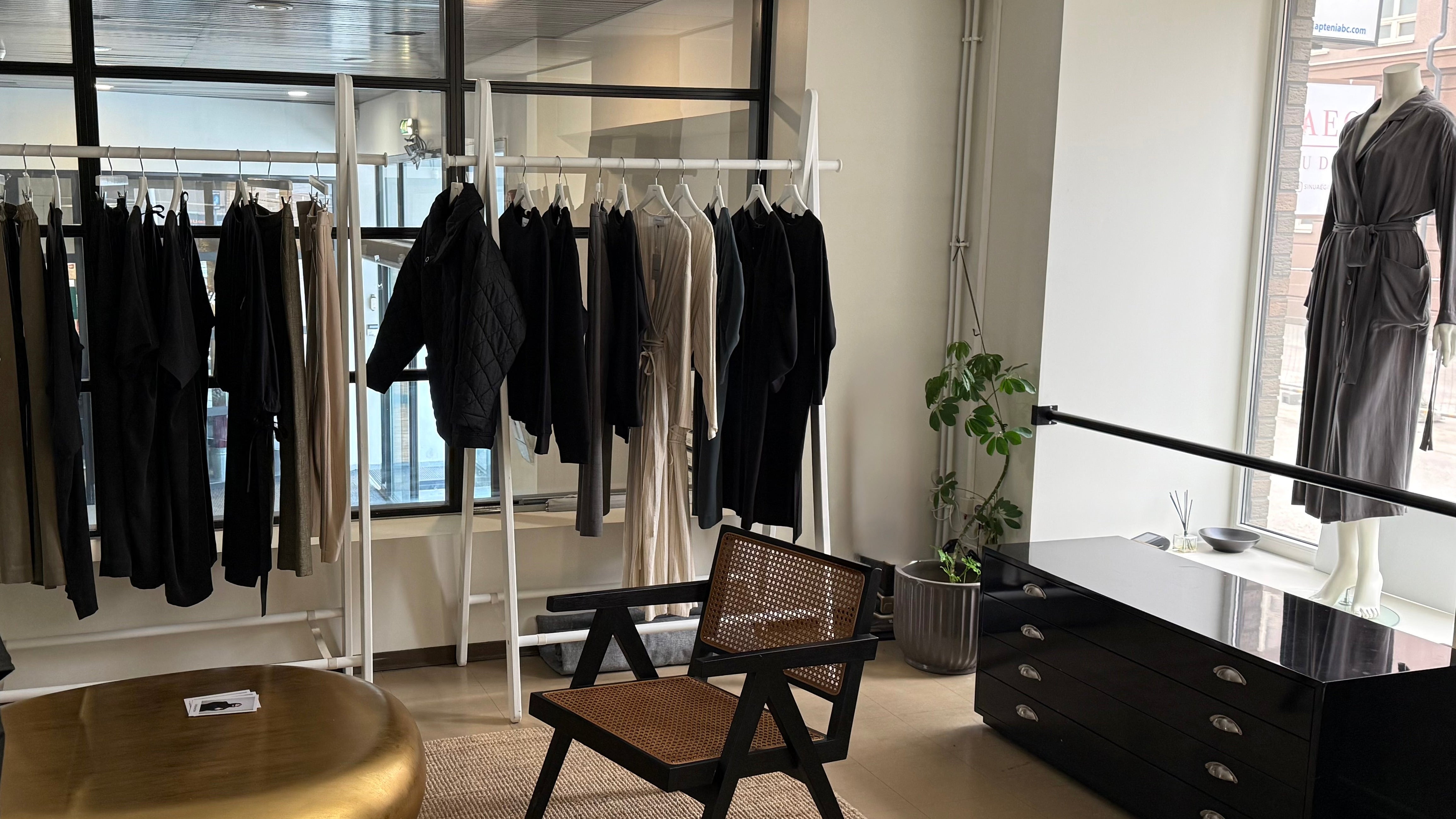 Clothing rack with black outfits in a modern room with a chair and dresser.