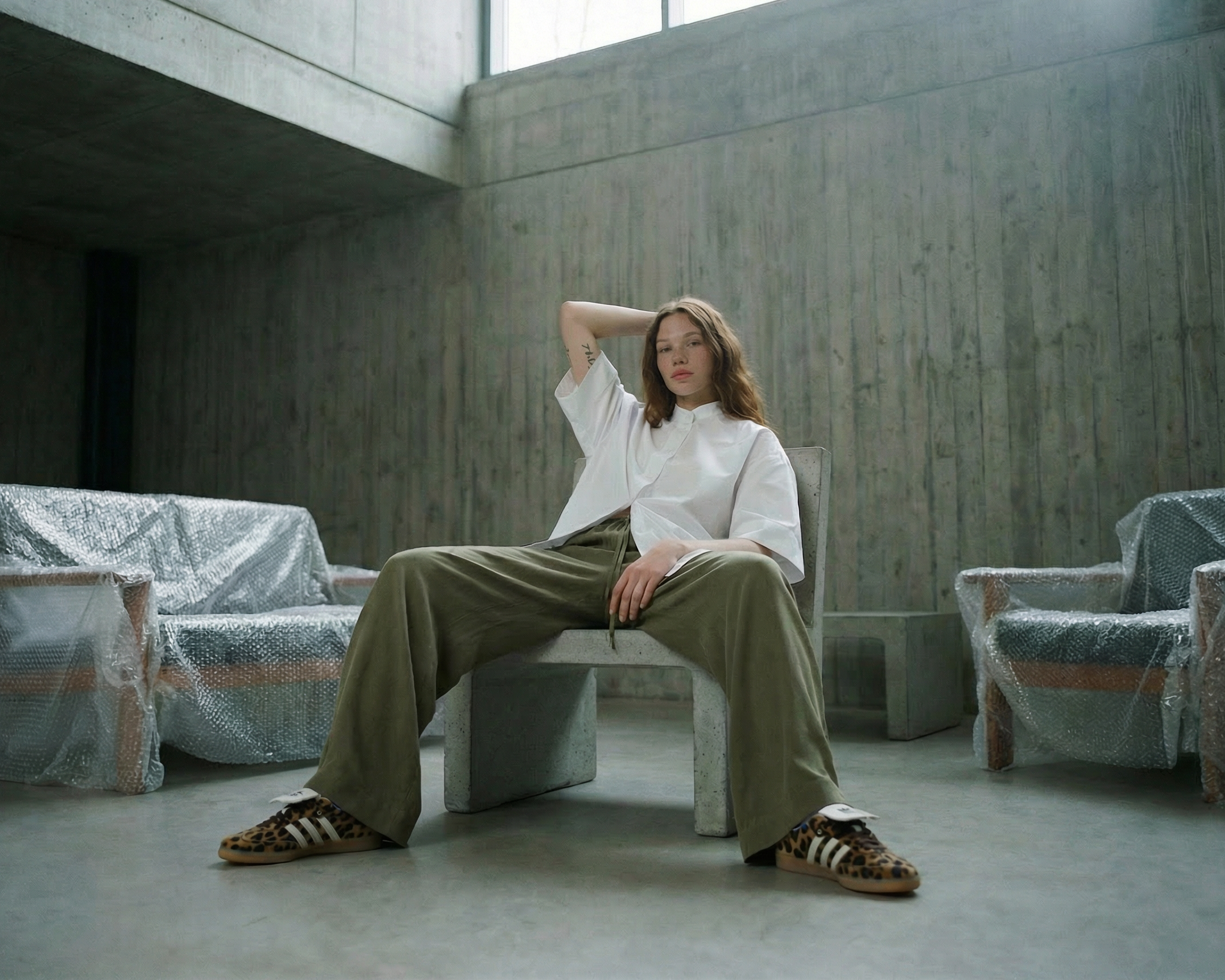Person sitting on a bench in a minimalist room with concrete walls and floor.