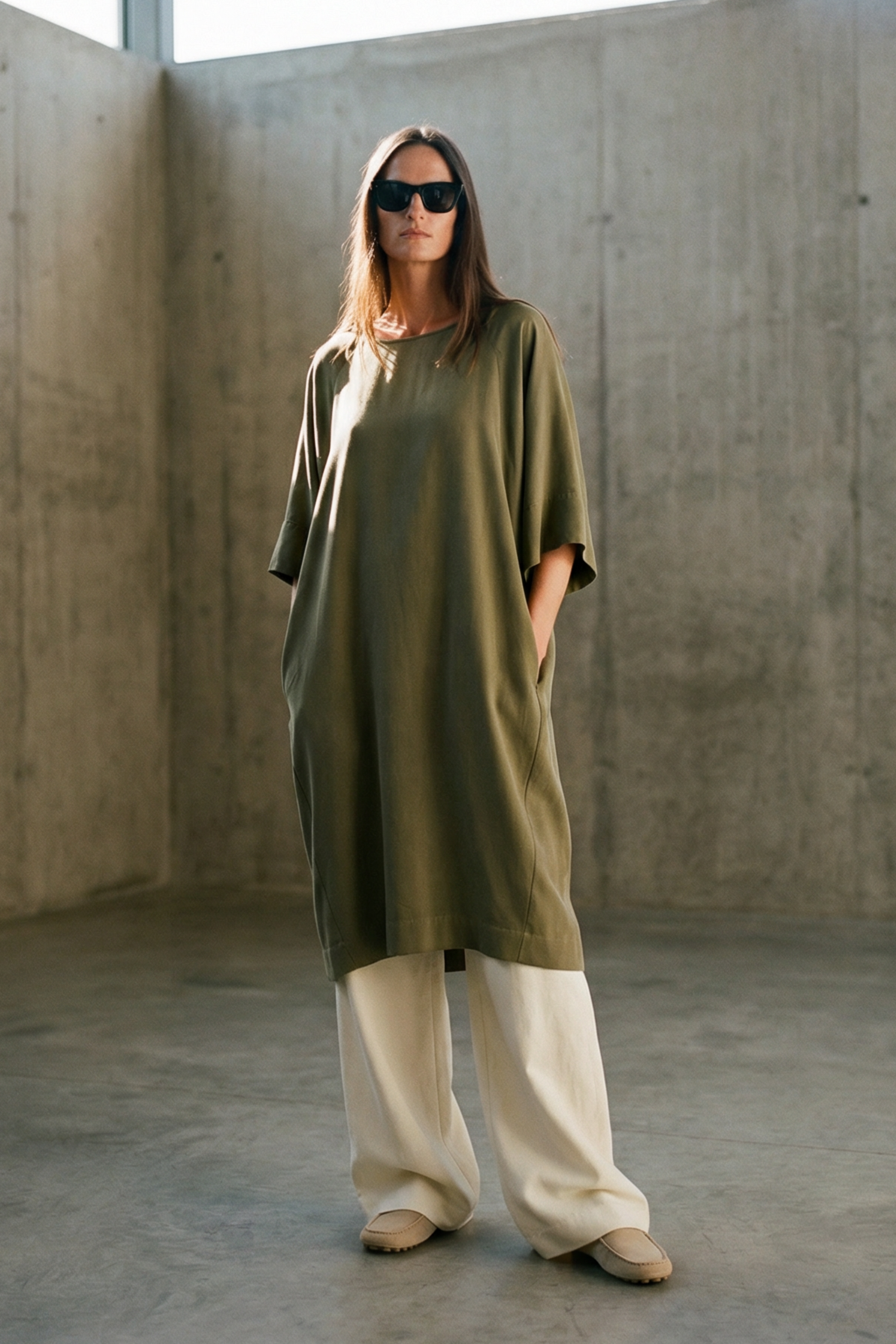 Woman wearing a green dress and sunglasses in a concrete room