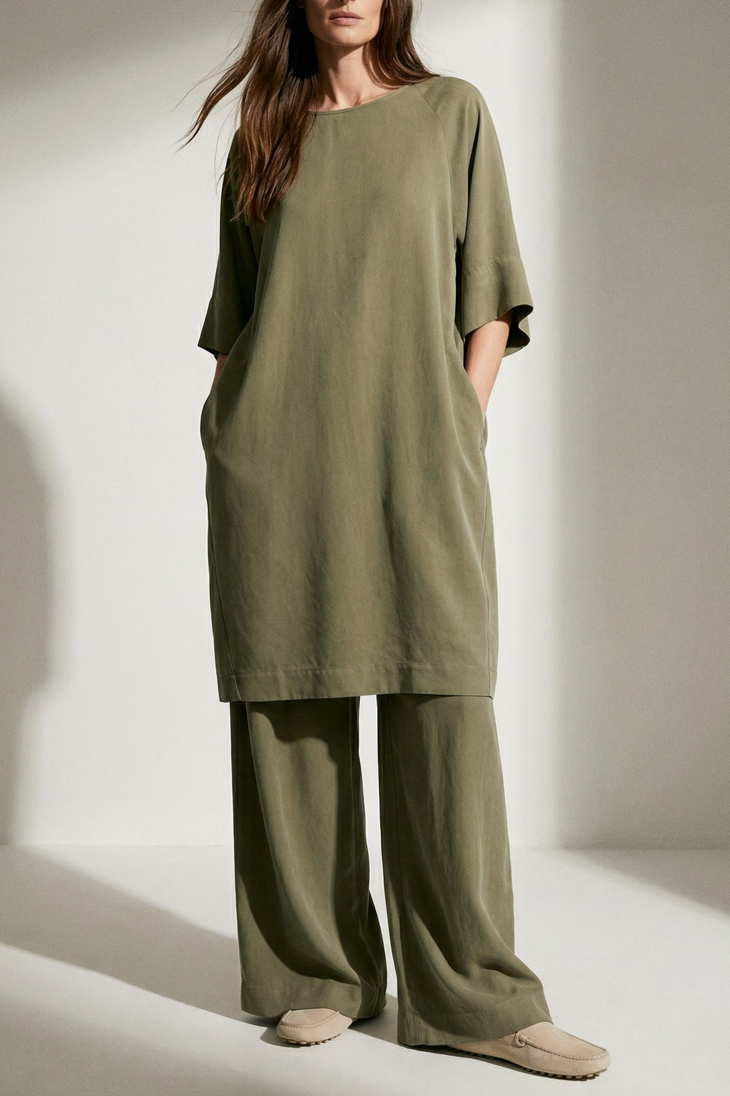 Woman wearing a green dress and pants set against a neutral background