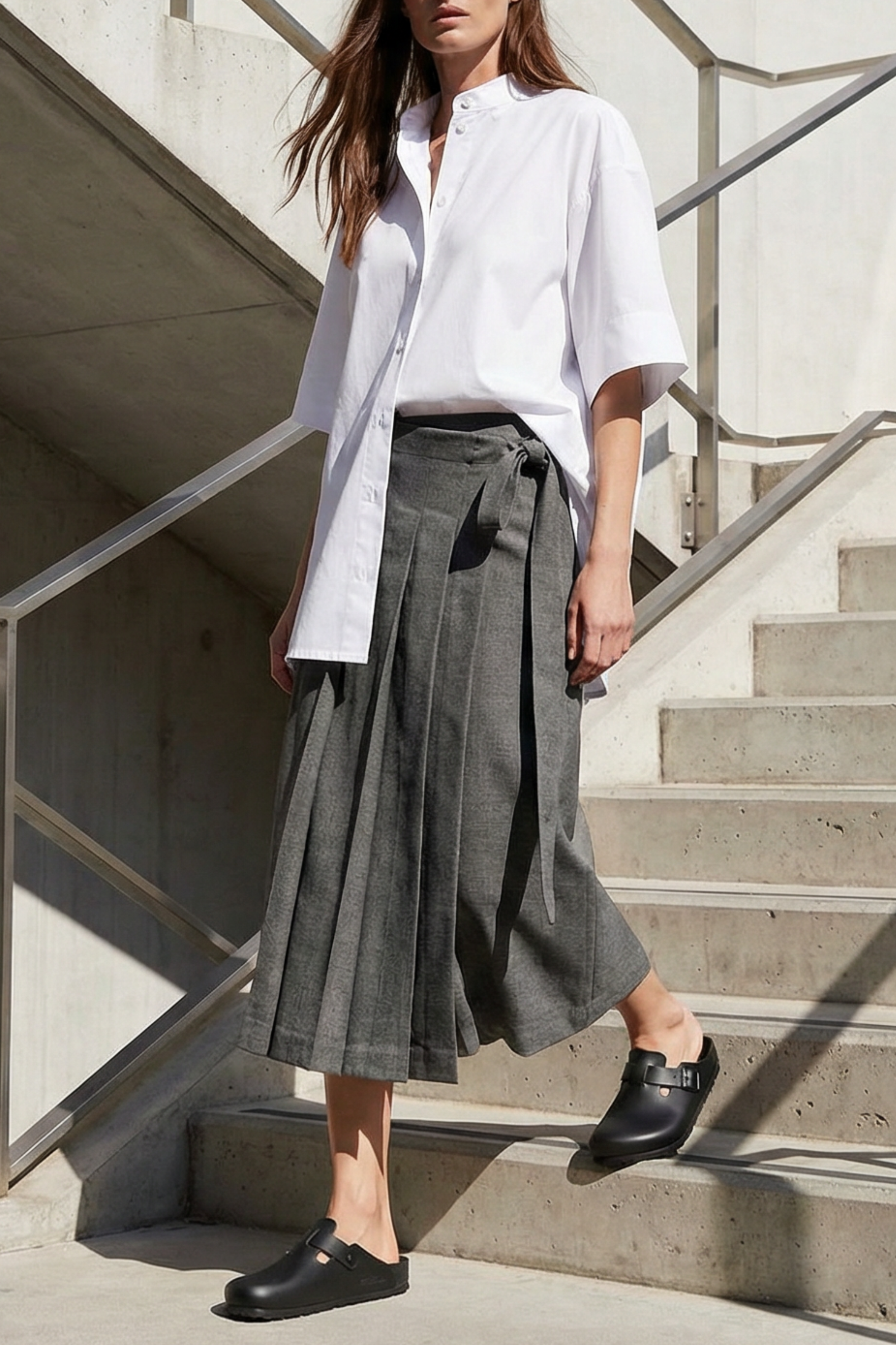 Woman in a white shirt and gray skirt walking on concrete steps.