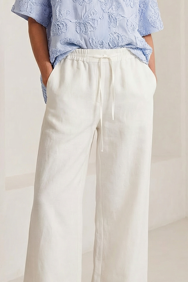 Woman wearing a light blue shirt and white pants in a minimalistic setting