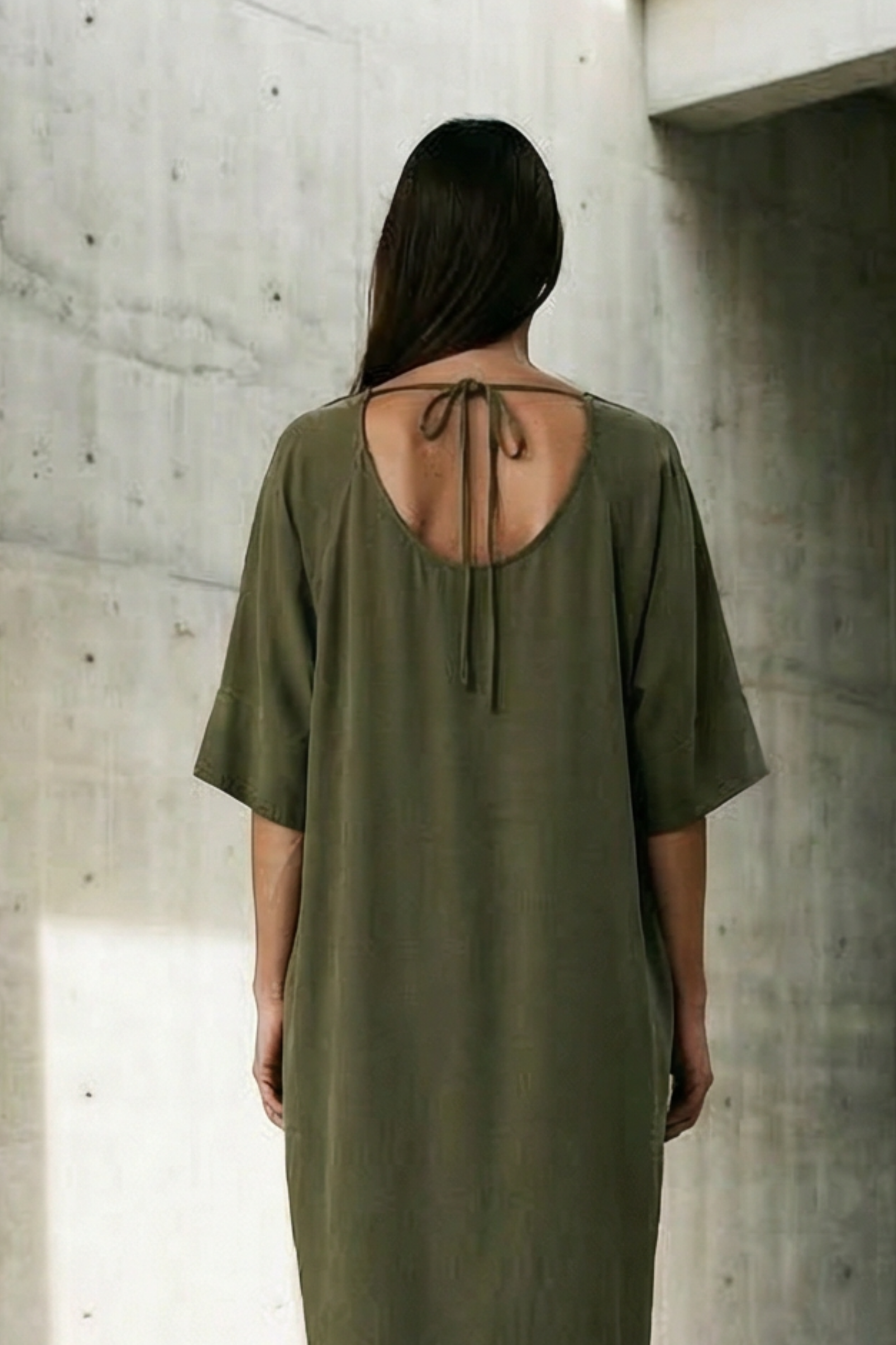 Person wearing a green dress standing in a concrete architectural space with light filtering through.