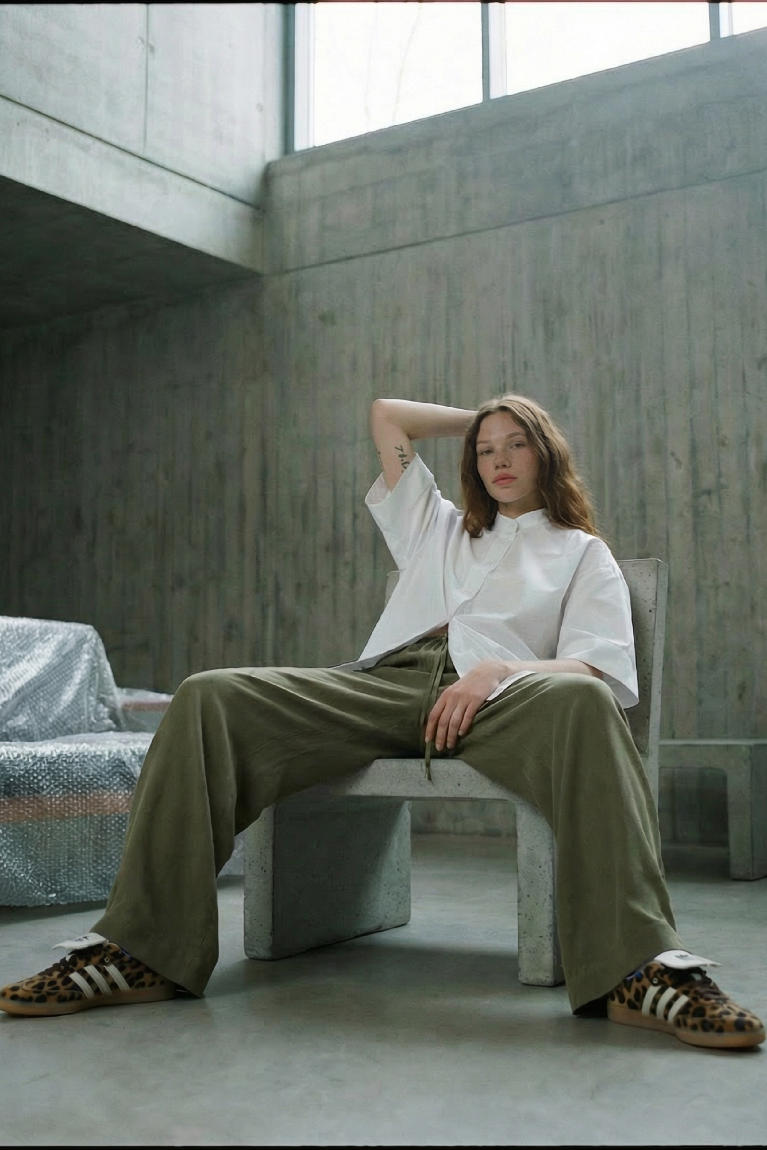 Person sitting on a bench in a minimalist room with concrete walls and floor.
