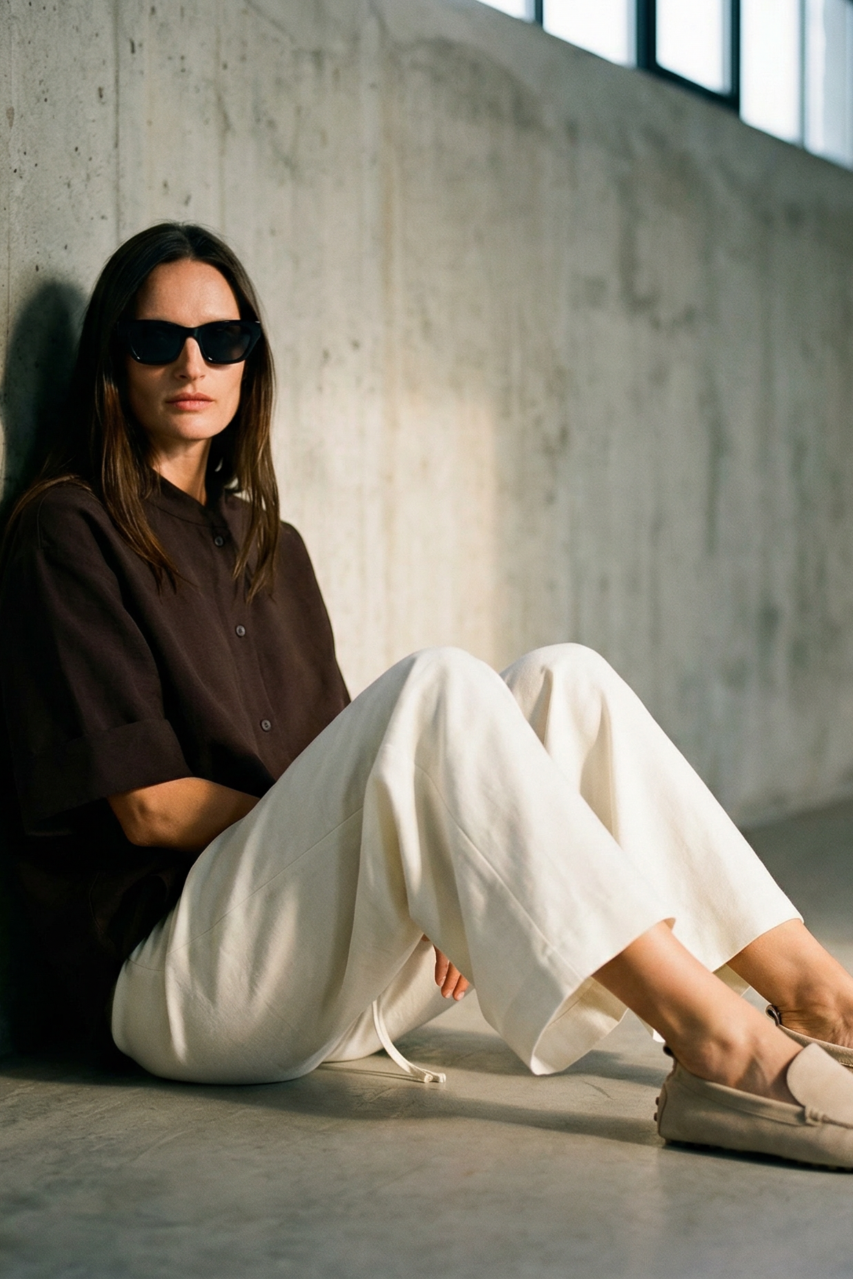 Person sitting against a concrete wall wearing sunglasses and casual clothing.